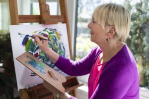 Happy retired woman painting on canvas for fun at home