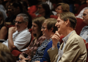 people smiling in theater seats listening to presenter