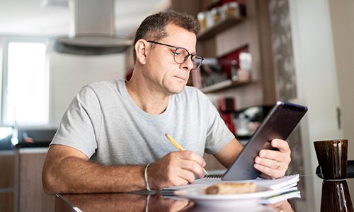 A man eats breakfast while working on his tablet computer.