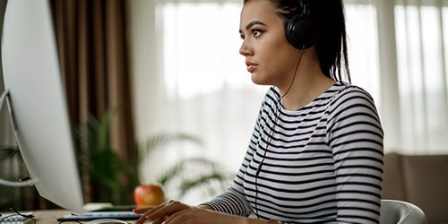 A woman in headphones works on a laptop.