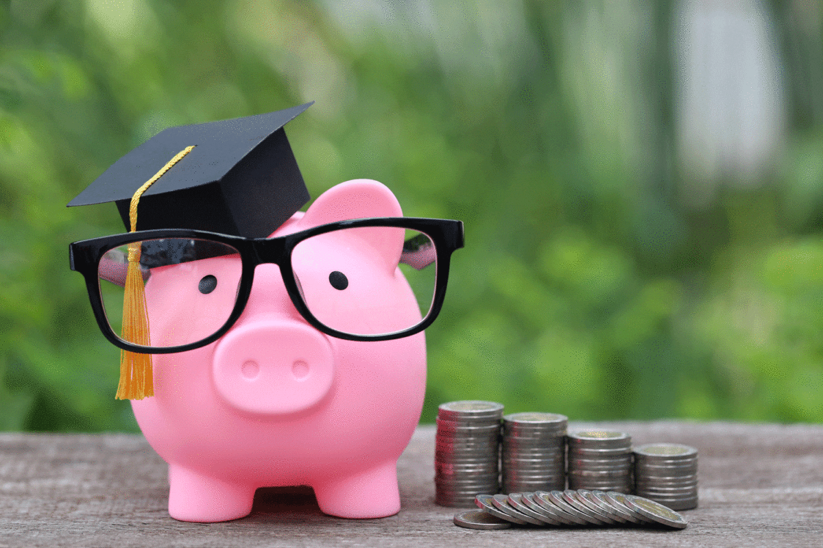 piggy bank wearing graduation cap next to stack of coins
