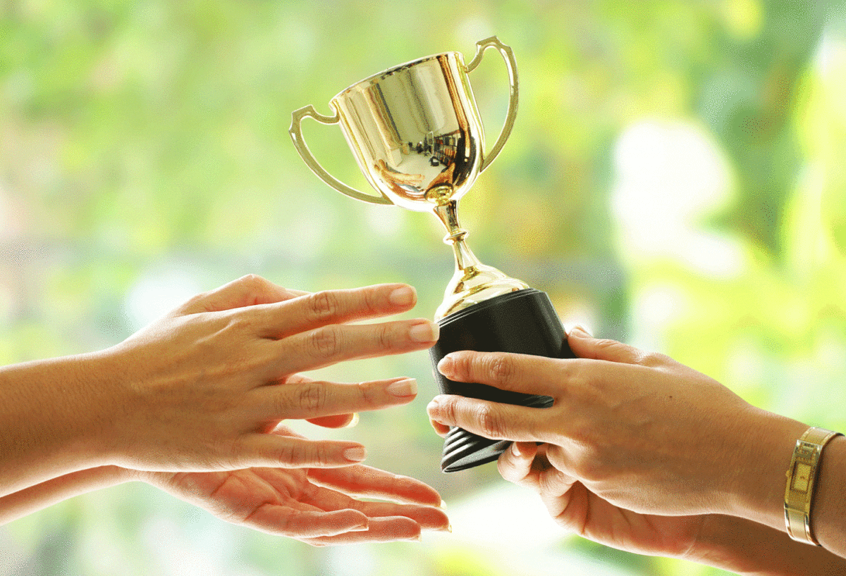 Set of one person's hands handing over a trophy to another person's hands