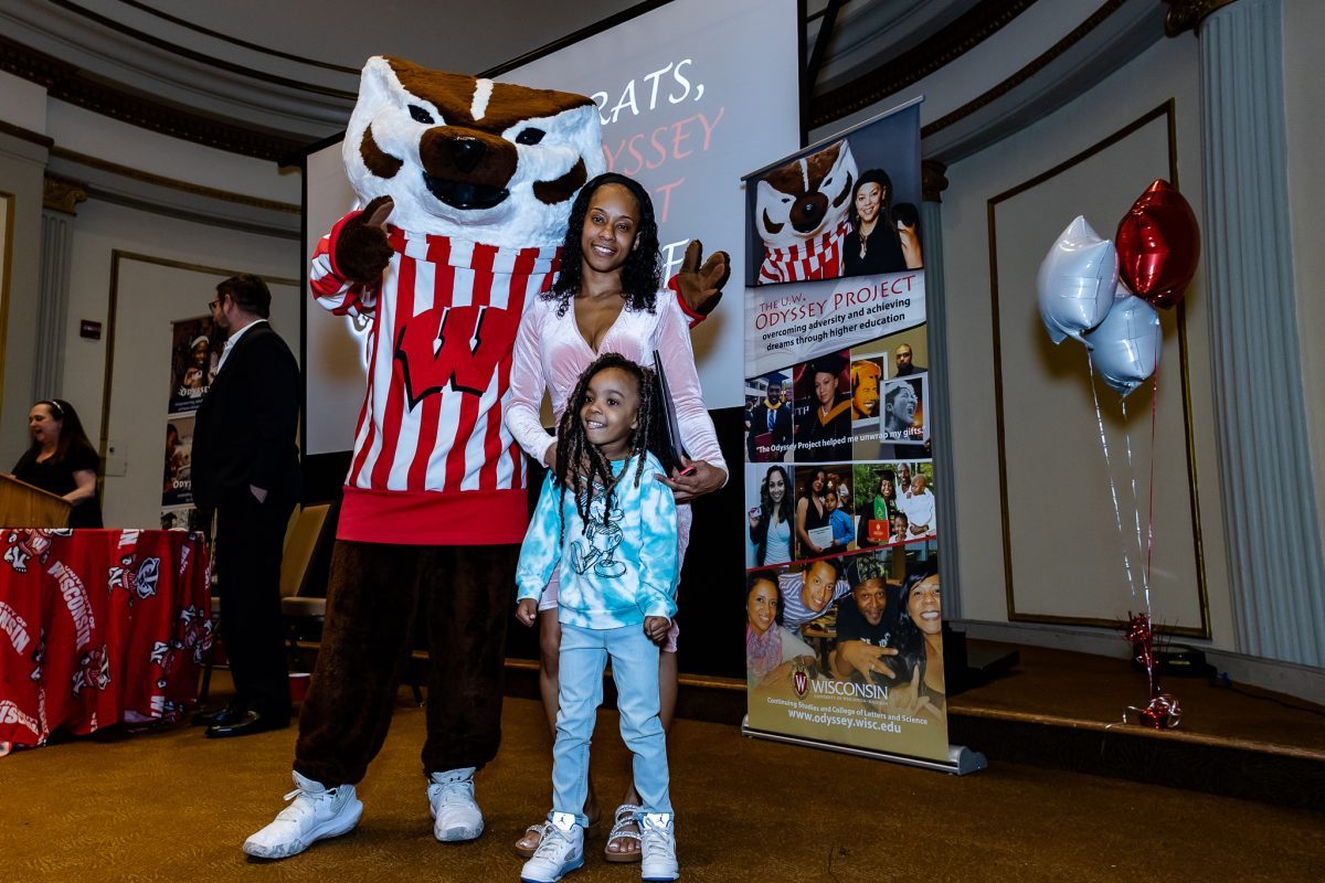 Odyssey graduate Yasmine Dobbins poses with her young daughter and Bucky Badger on stage at the graduation ceremony.