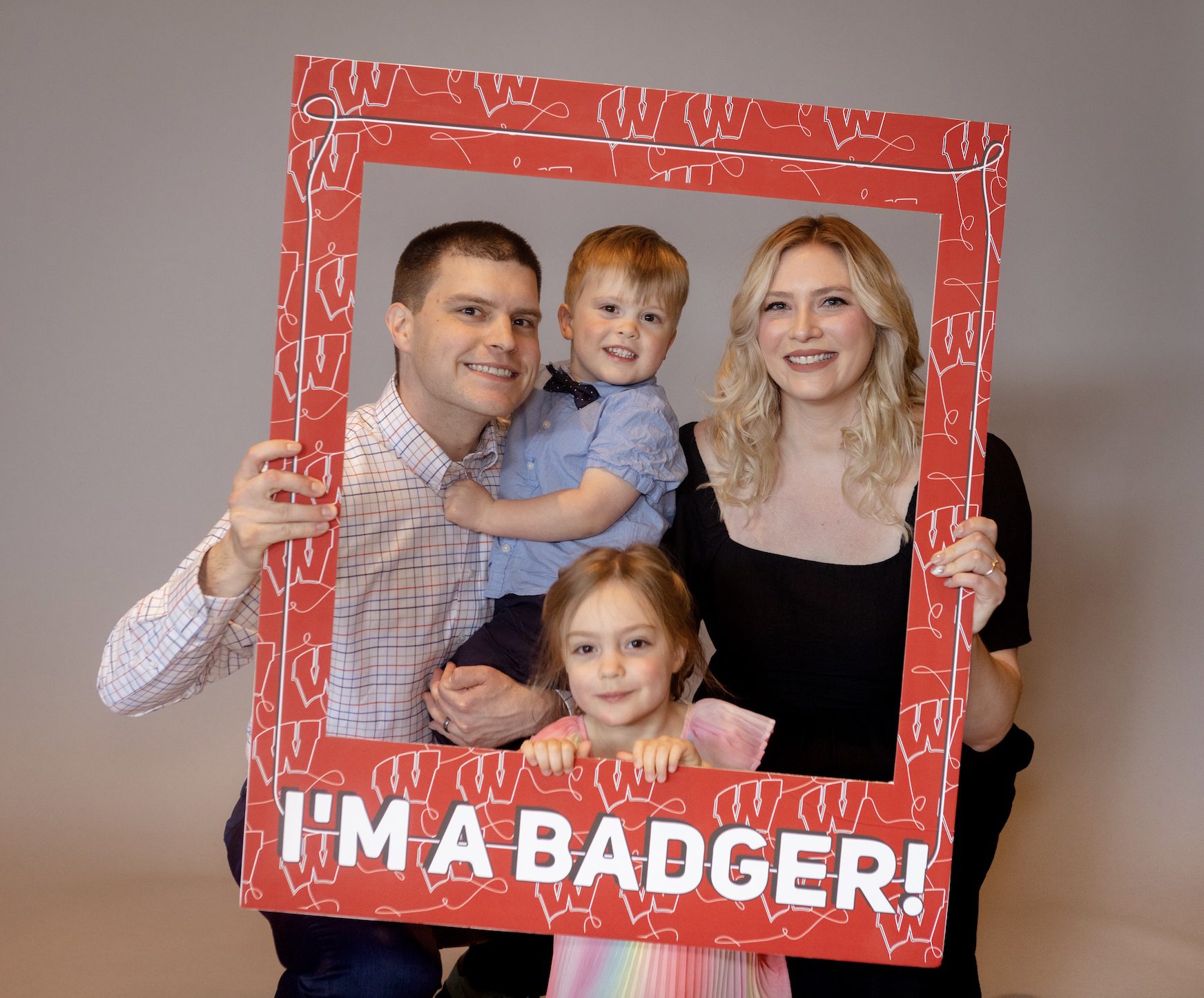 A husband, wife and their two kids smiling behind a sign that says "I'm A Badger!"