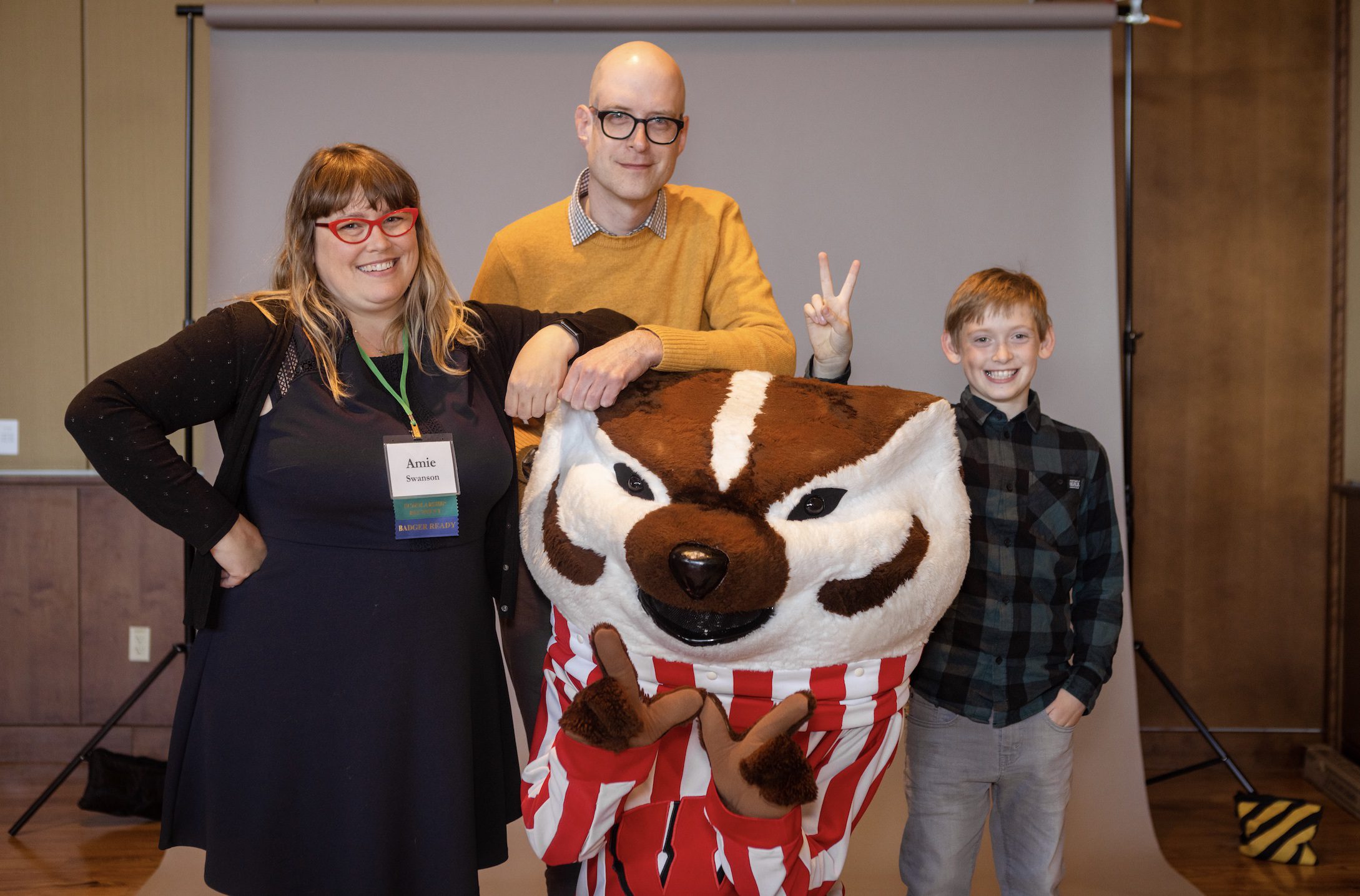 A wife, husband and their son posing with Bucky the Badger