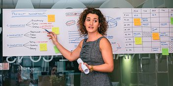 Woman in office setting pointing to words and post-its on a whiteboard