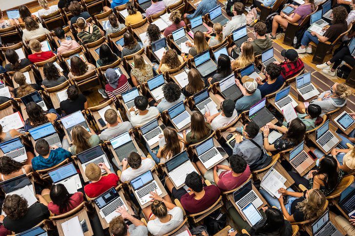 An aerial view of UW–Madison students sitting in rows in lecture hall at desks with open laptops.