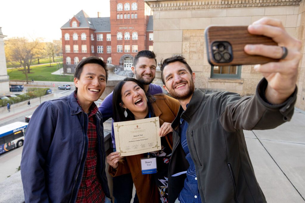 Student surrounded by 3 guests poses for selfie with Badger Ready certificate