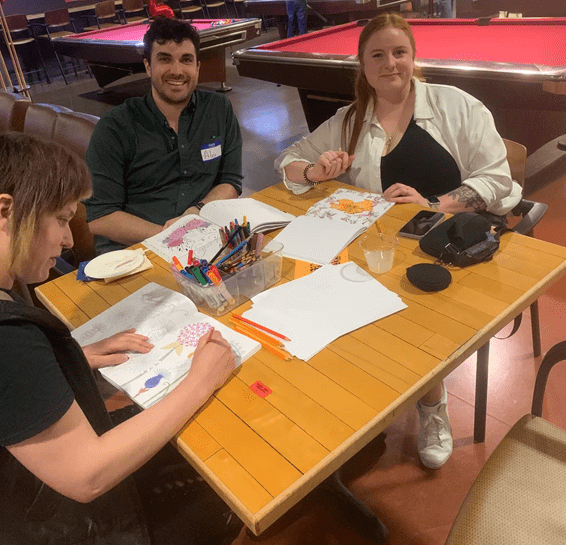 three students sitting a table, coloring