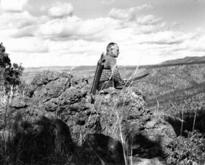 Aldo Leopold sitting on the edge of a rock, looking out over the land