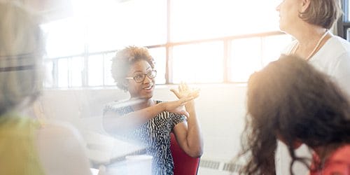 In a sunny conference room, a woman talks animatedly with her colleagues.