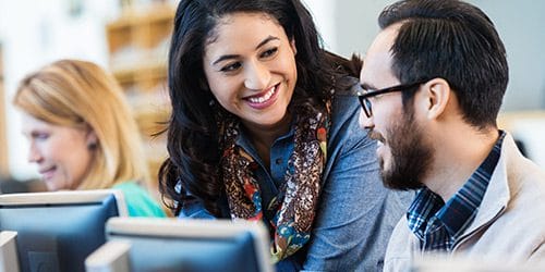 Smiling woman helping coworker on computer