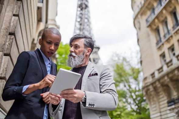 Two business people discussing something on the screen of an iPad on a Parisian street.