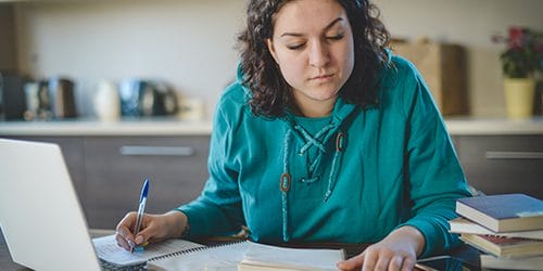 A student reads notes in front of a laptop.