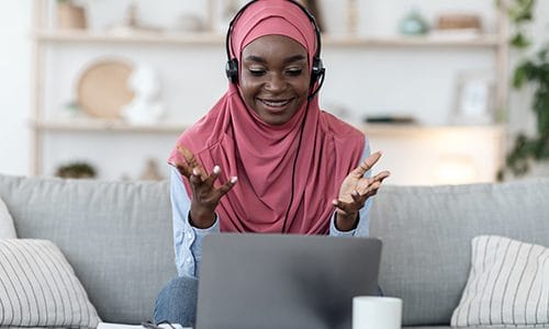 A woman in a headscarf talks animated at her computer during online class