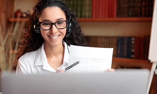 A woman points to her notes during an online meeting.